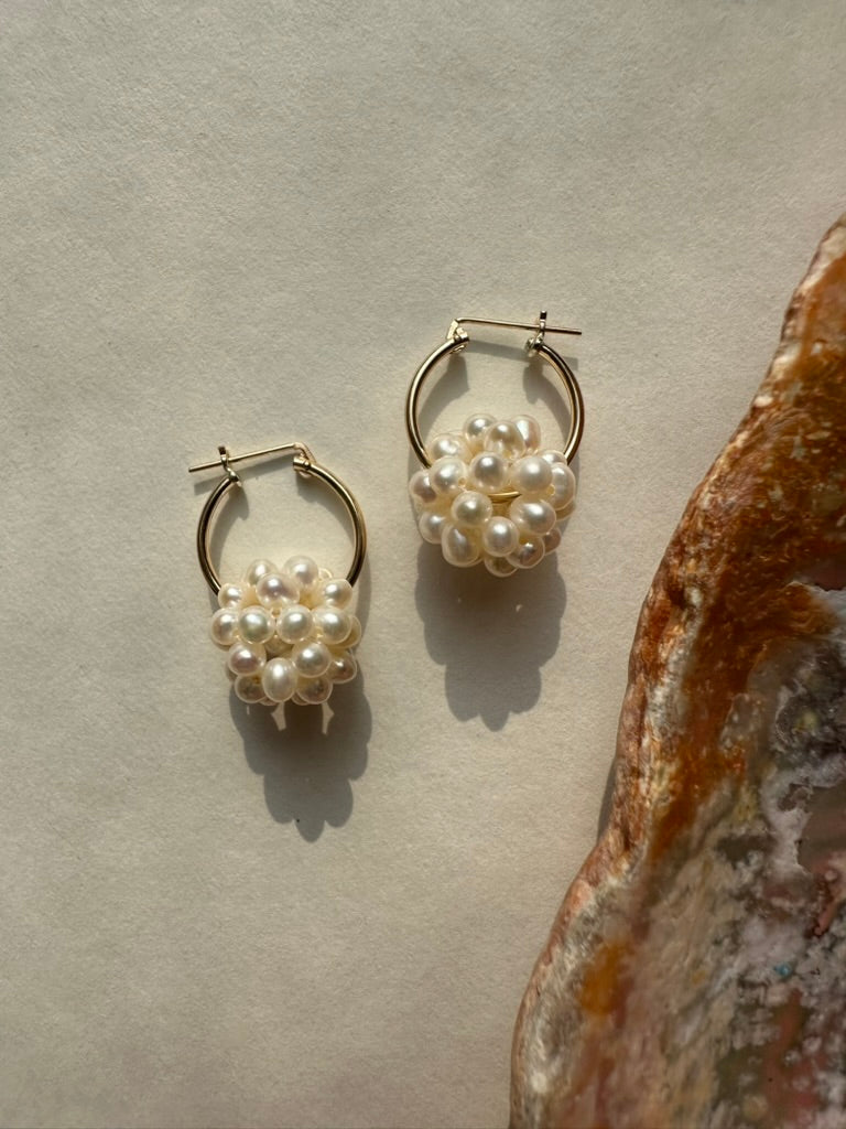 Pair of pearl hoop earrings on a textured surface with a seashell