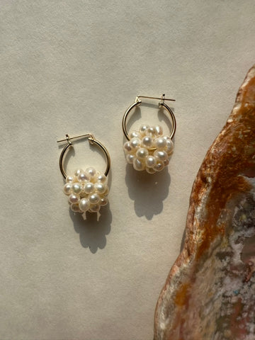 Pair of pearl hoop earrings on a textured surface with a seashell