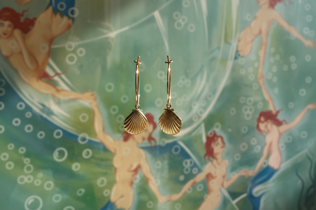 Gold shell earrings held up against a mermaid-themed background
