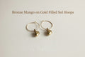 Gold hoop earrings with small dangling elements on a light gray background