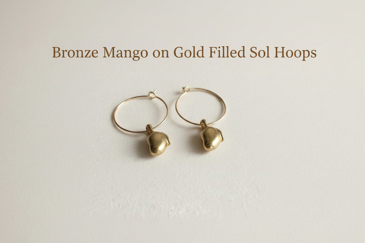 Gold hoop earrings with small dangling elements on a light gray background
