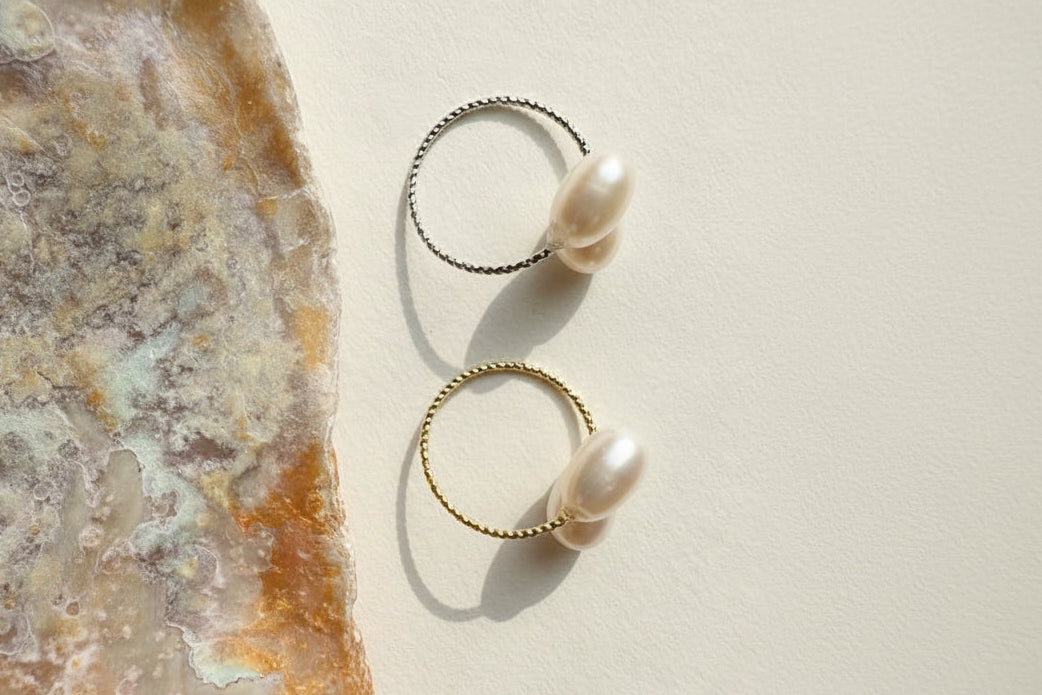 Two gold rings with pearls on a textured stone surface