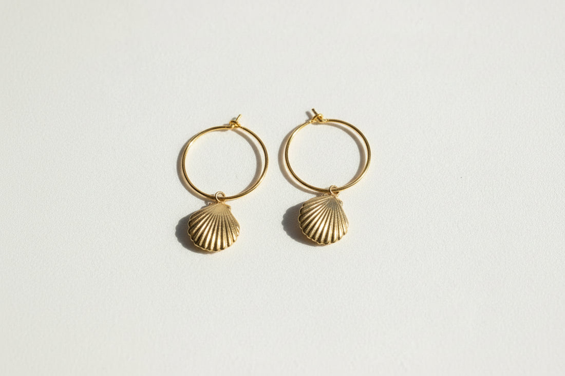 Gold hoop earrings with shell designs on a beige background