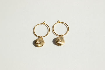 Gold hoop earrings with shell designs on a beige background