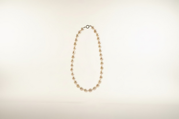 Pearl necklace on a light gray surface with an oyster shell.