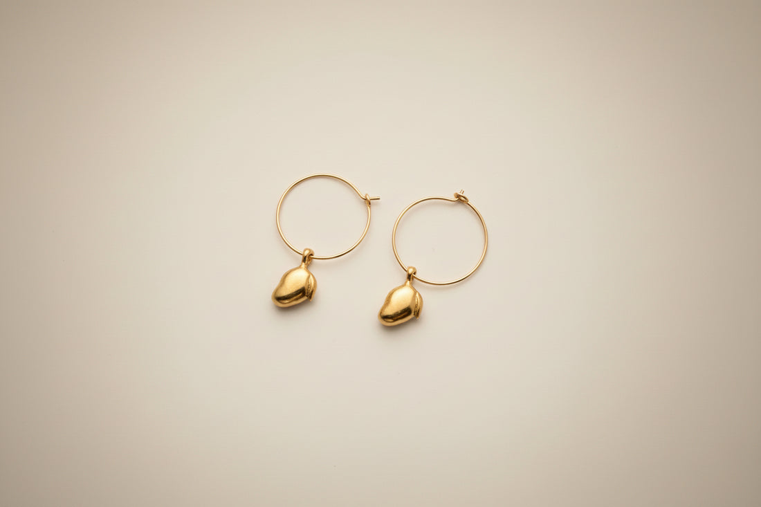 Gold hoop earrings with handcarved mango pendants on a light cream background by xomango