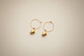Gold hoop earrings with handcarved mango pendants on a light cream background by xomango