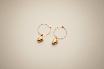 Gold hoop earrings with handcarved mango pendants on a light cream background by xomango