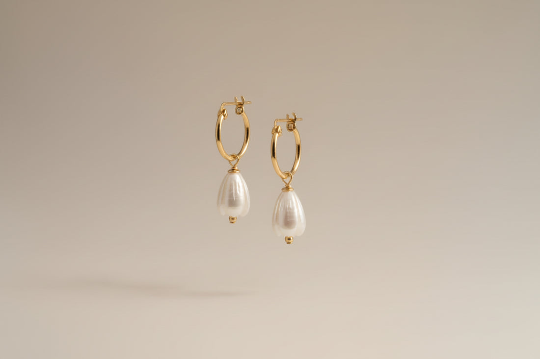 Gold hoop earrings with pearl drops on a warm cream background