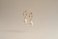 Gold hoop earrings with pearl drops on a warm cream background