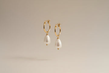 Gold hoop earrings with pearl drops on a warm cream background