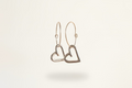 Hand carved Heart-shaped charms hanging from dainty gold hoops against neutral background