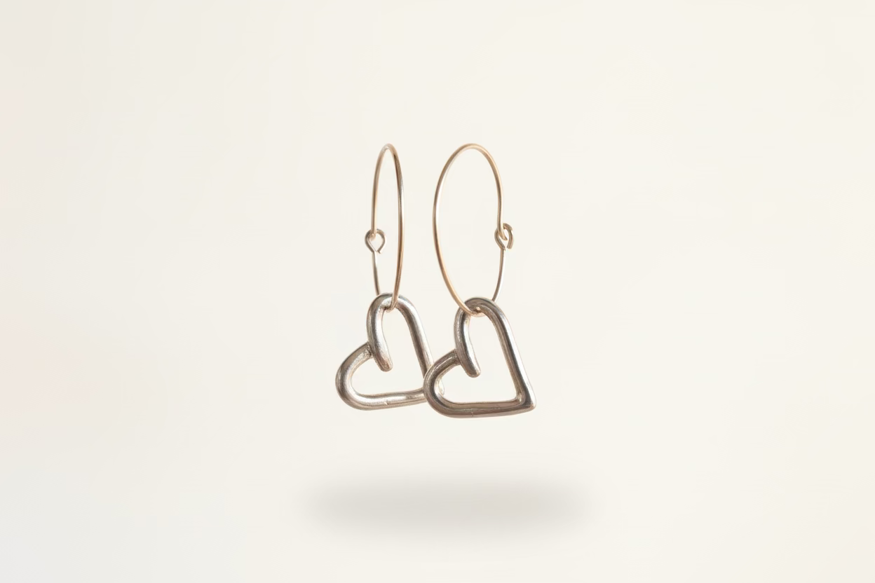 Hand carved Heart-shaped charms hanging from dainty gold hoops against neutral background