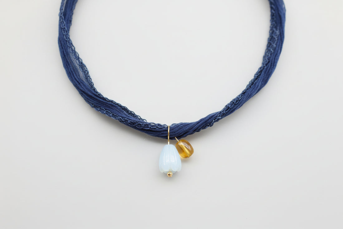 Tahitian pearl, mother of pearl Pikake flower, and amber bead hang from a denim blue silk ribbon necklace by xomango