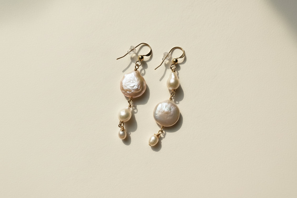 Pearl earrings on a textured beige surface with a shell in the foreground