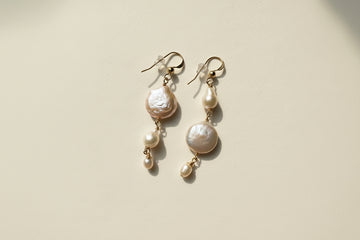 Pearl earrings on a textured beige surface with a shell in the foreground