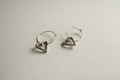 Silver hoop earrings with heart-shaped charms on a light gray background
