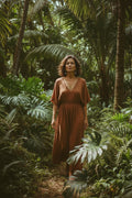 Woman in a rust-colored dress standing in a lush tropical forest