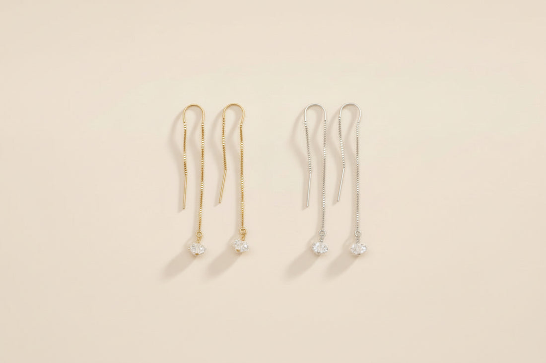 Two pairs of gold and silver herkimer diamond threader earrings on a beige background