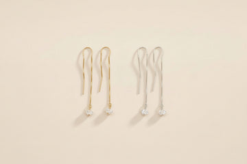 Two pairs of gold and silver herkimer diamond threader earrings on a beige background