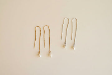 Two pairs of gold earrings on a beige background